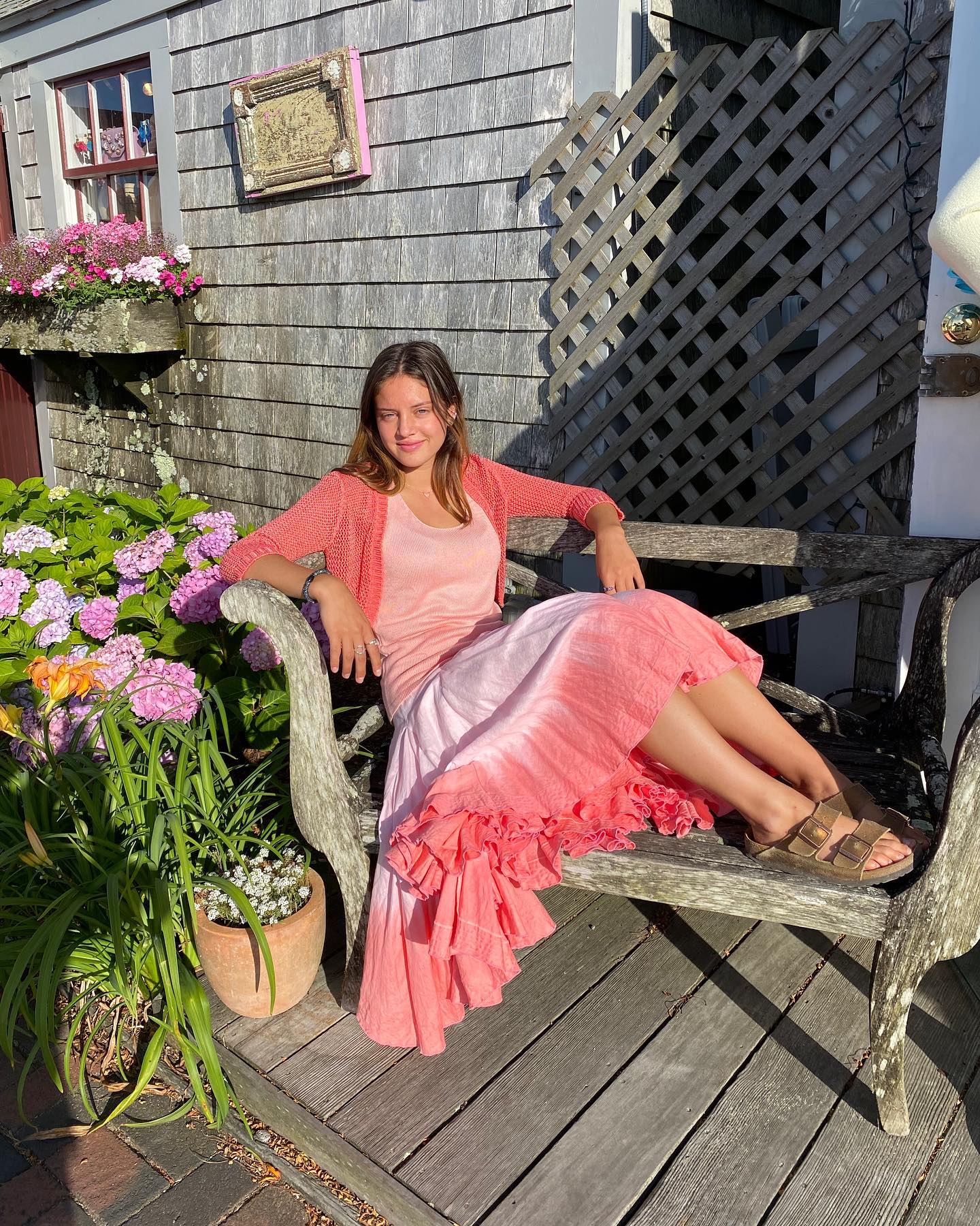 A woman in a coral knit and dip-dyed skirt on a weathered bench