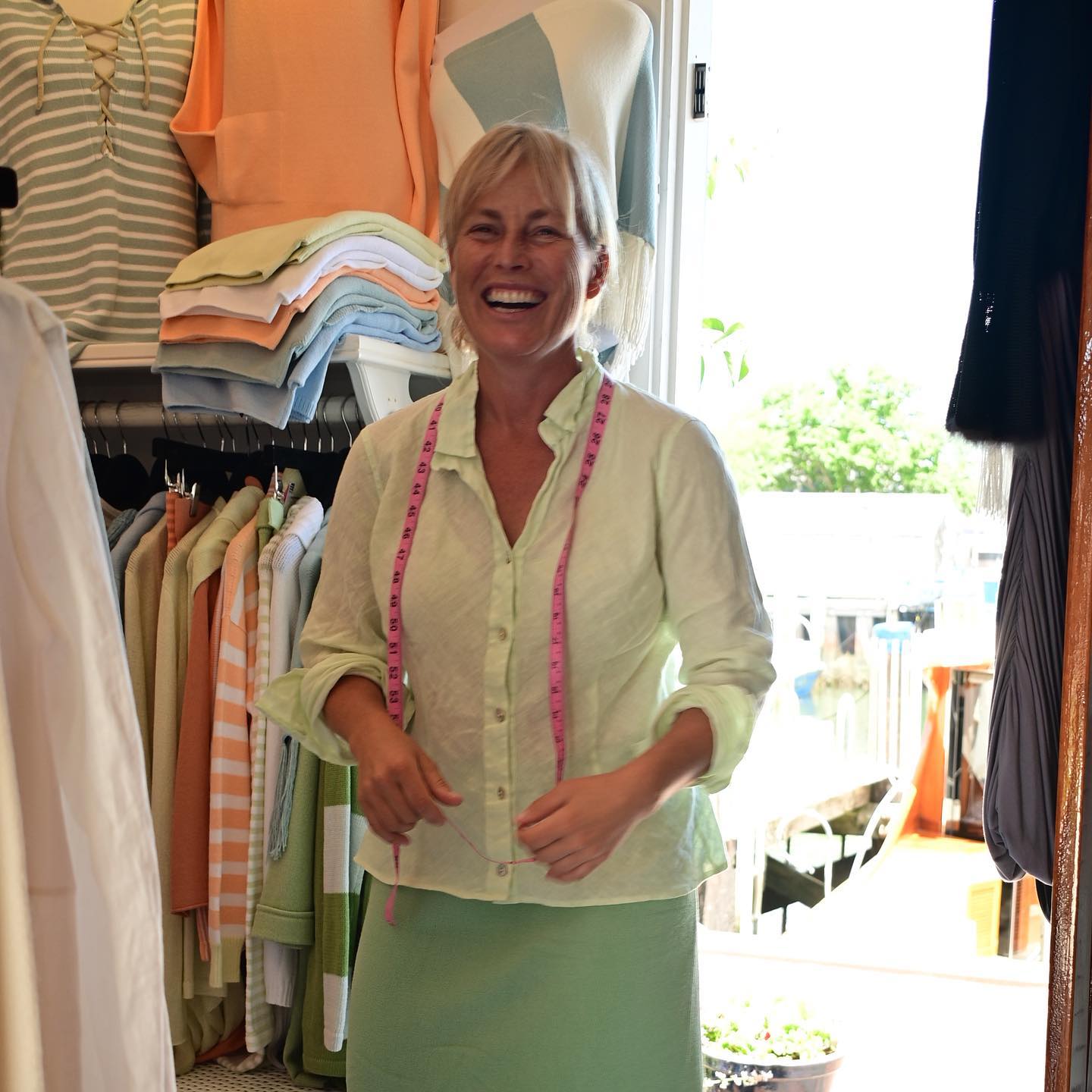 Kari laughing in the shop, a pink tape measure around her neck